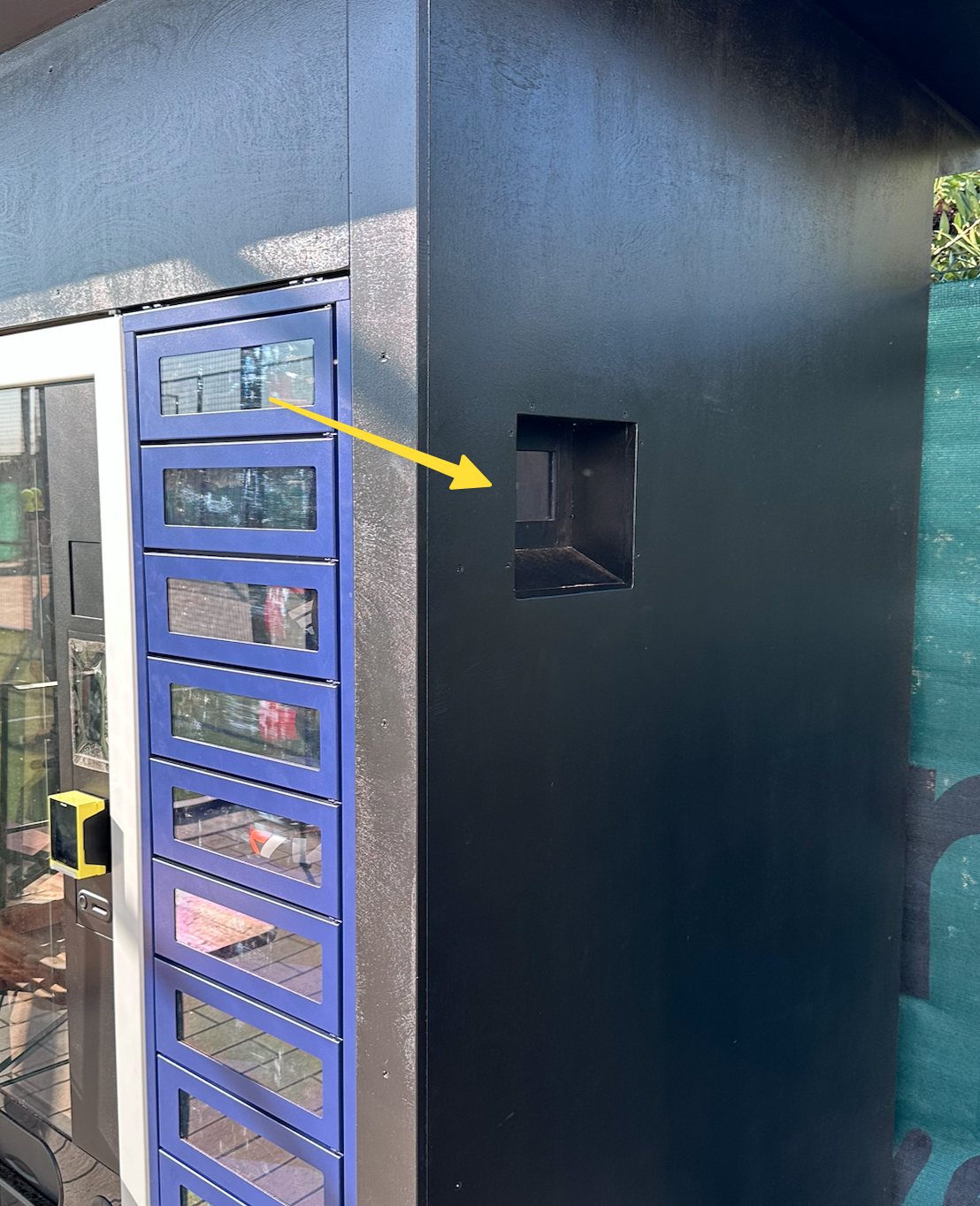Der Equipment-Automat von der Seite, ein gelber Pfeil zeigt auf die Nische mit dem Display an der rechten Seitenwand
